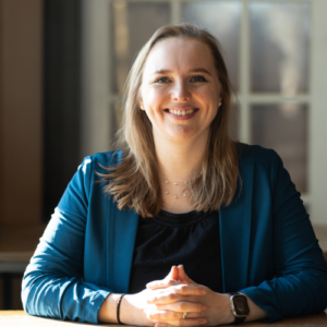 Photo of a woman with blonde hair wearing a blue blazer, smiling with crossed hands